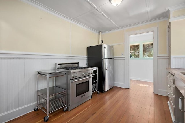 kitchen with appliances with stainless steel finishes, crown molding, and wood-type flooring