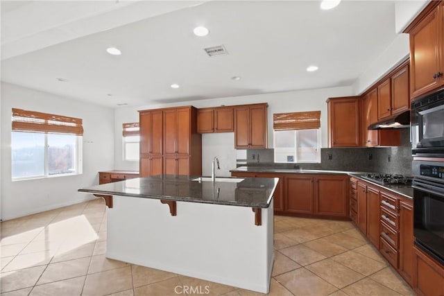 kitchen with sink, an island with sink, dark stone counters, a kitchen bar, and black appliances