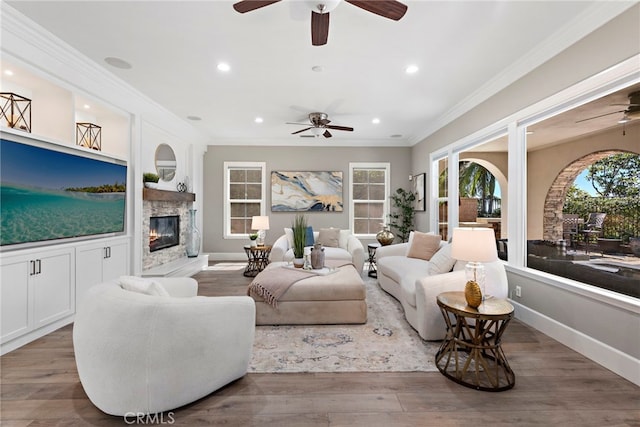 living room featuring crown molding, ceiling fan, a stone fireplace, and hardwood / wood-style floors