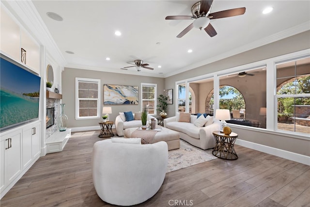 living room with crown molding, a stone fireplace, and light hardwood / wood-style flooring