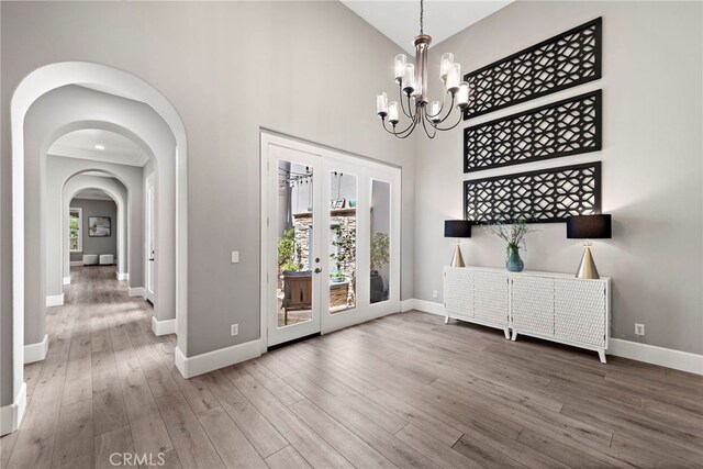 entrance foyer with french doors, a towering ceiling, hardwood / wood-style flooring, and a notable chandelier