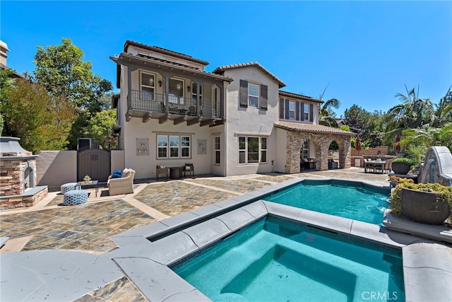 rear view of property with a balcony, a patio area, and a pool with hot tub