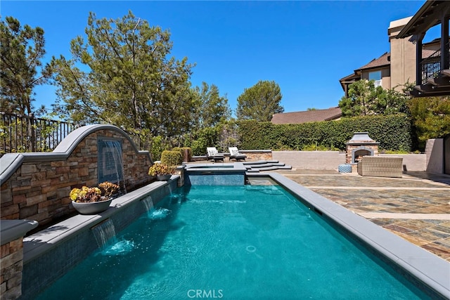 view of pool with an outdoor stone fireplace, pool water feature, and a patio area