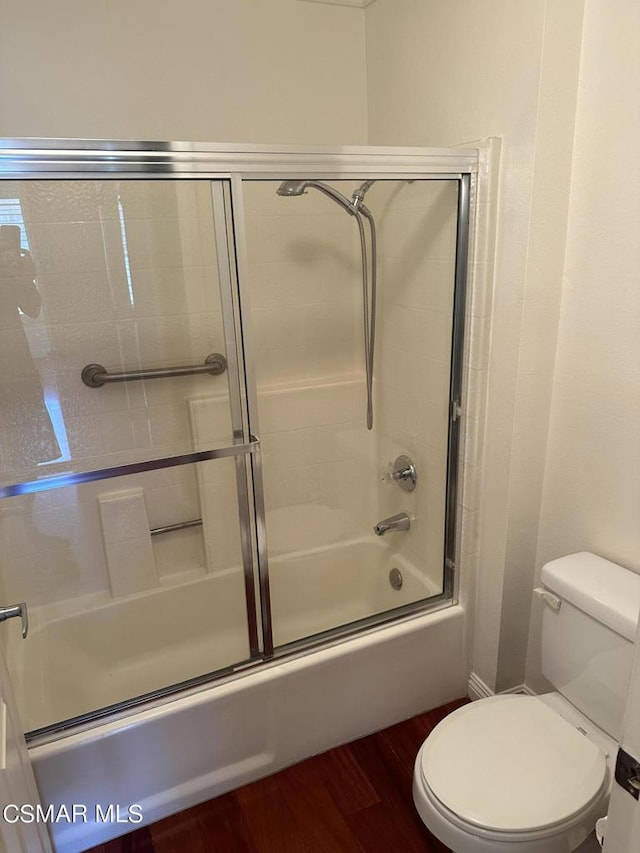 bathroom with wood-type flooring, toilet, and bath / shower combo with glass door