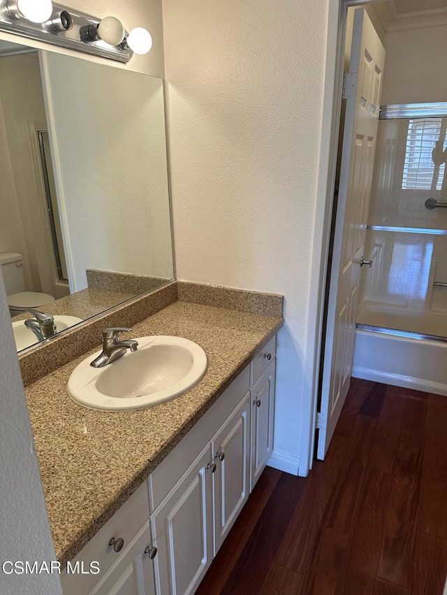 full bathroom featuring hardwood / wood-style floors, vanity, toilet, and combined bath / shower with glass door