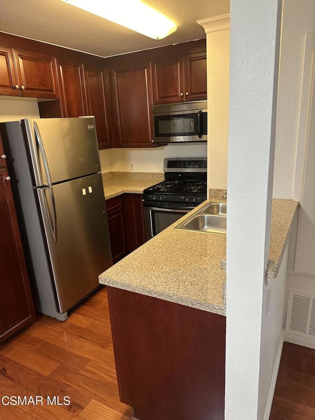 kitchen with sink, dark wood-type flooring, light stone counters, a textured ceiling, and appliances with stainless steel finishes