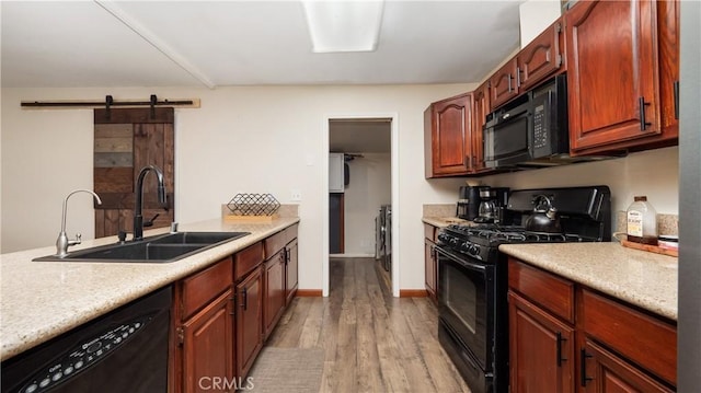 kitchen with a barn door, sink, black appliances, and light hardwood / wood-style floors