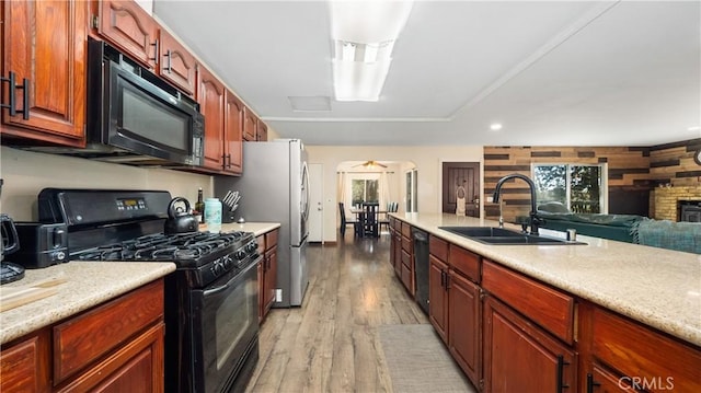 kitchen featuring sink, light hardwood / wood-style floors, a brick fireplace, and black appliances