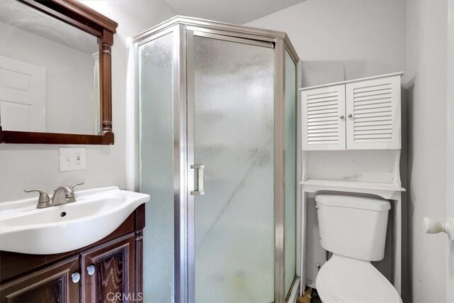 bathroom featuring a shower with door, vanity, and toilet