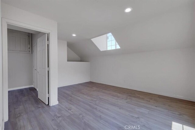 additional living space featuring vaulted ceiling with skylight and light hardwood / wood-style flooring