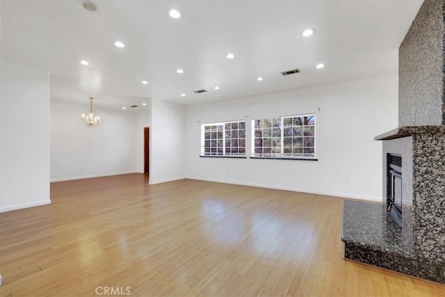 unfurnished living room with light wood-type flooring, a chandelier, and a premium fireplace