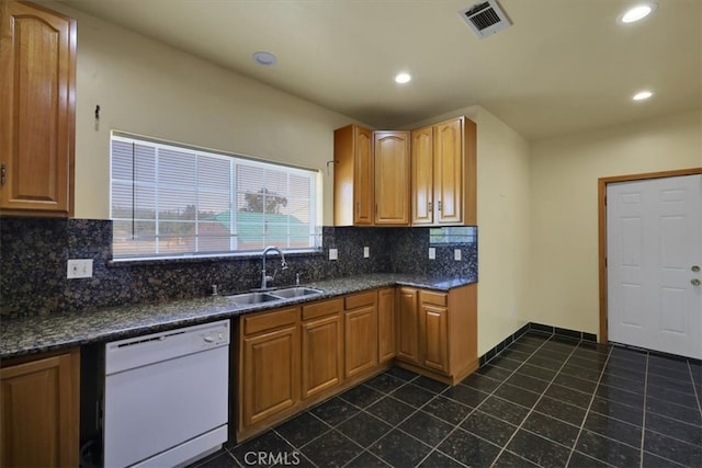 kitchen with dark tile patterned floors, dark stone counters, dishwasher, sink, and backsplash