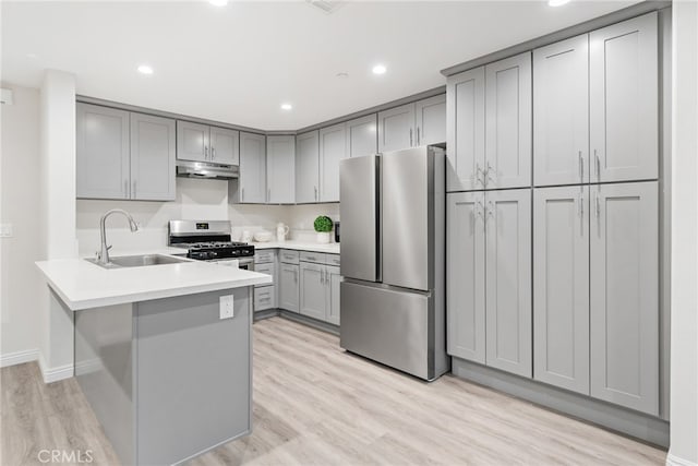 kitchen with appliances with stainless steel finishes, kitchen peninsula, gray cabinets, light hardwood / wood-style flooring, and sink