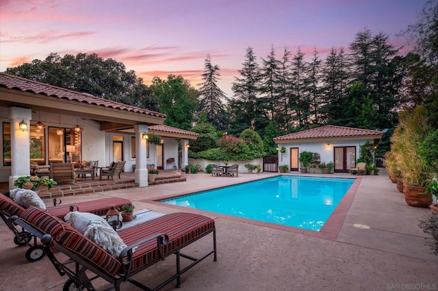 pool at dusk featuring a patio area and an outdoor structure