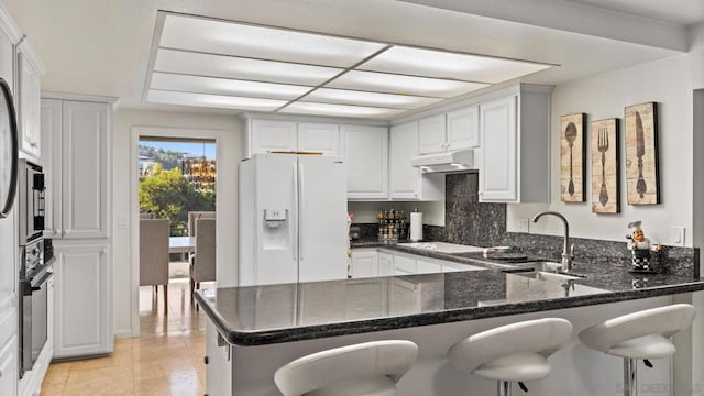 kitchen with white cabinets, sink, kitchen peninsula, dark stone countertops, and white fridge with ice dispenser