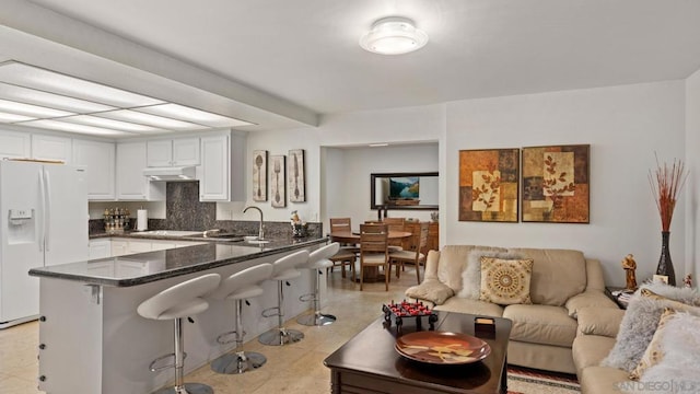 kitchen featuring a kitchen breakfast bar, white refrigerator with ice dispenser, white cabinets, kitchen peninsula, and sink