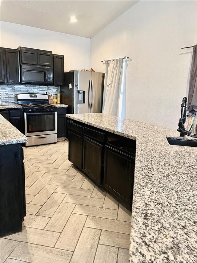 kitchen with light stone countertops, tasteful backsplash, stainless steel appliances, sink, and light parquet flooring