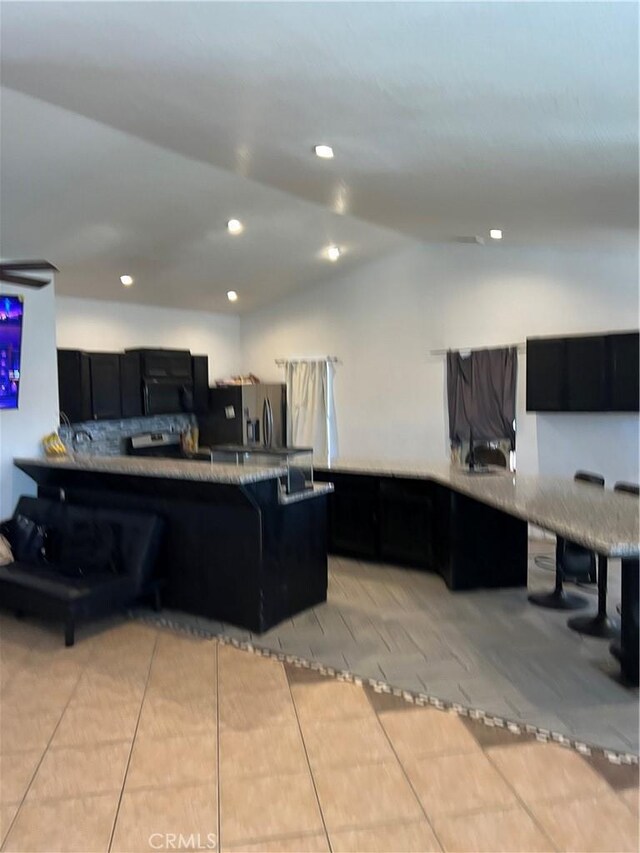 kitchen with stainless steel fridge with ice dispenser, kitchen peninsula, vaulted ceiling, a breakfast bar area, and light tile patterned floors