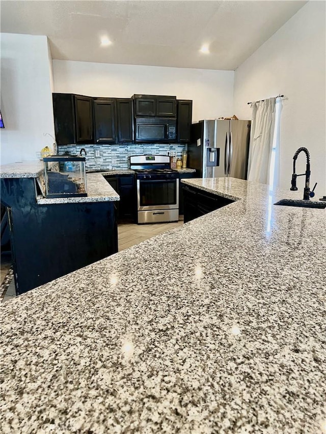 kitchen featuring tasteful backsplash, light stone counters, sink, and appliances with stainless steel finishes