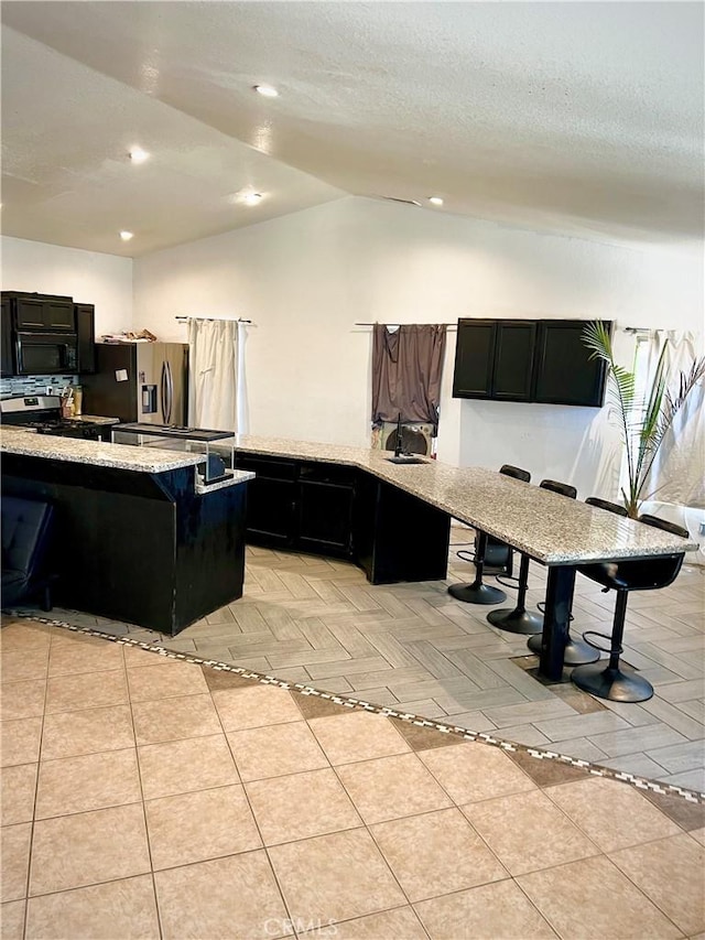 kitchen with light parquet flooring, stainless steel appliances, a breakfast bar area, and vaulted ceiling