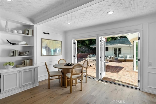 dining area featuring beamed ceiling, built in shelves, and light wood-type flooring