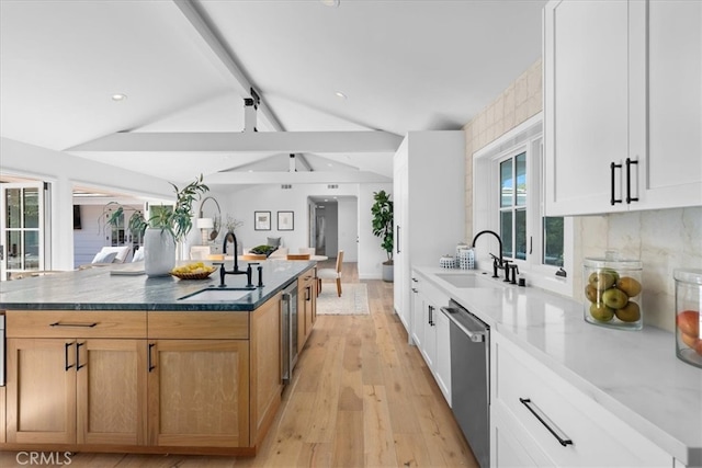 kitchen with white cabinets, stainless steel dishwasher, sink, and a large island with sink