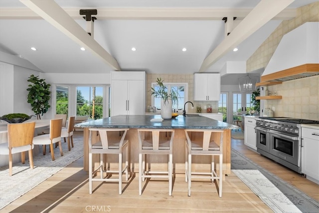 kitchen featuring a large island with sink, white cabinets, vaulted ceiling with beams, and double oven range