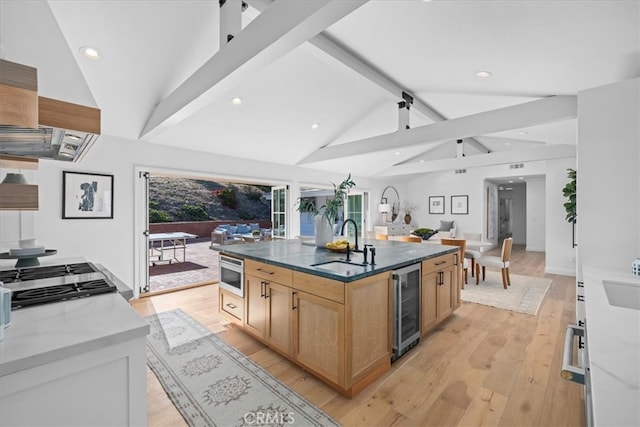 kitchen featuring vaulted ceiling with beams, light hardwood / wood-style flooring, a center island with sink, wine cooler, and sink