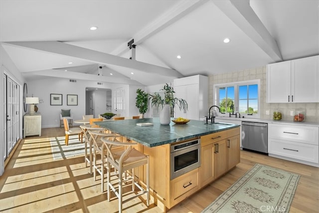 kitchen with appliances with stainless steel finishes, white cabinetry, light hardwood / wood-style floors, and a large island with sink