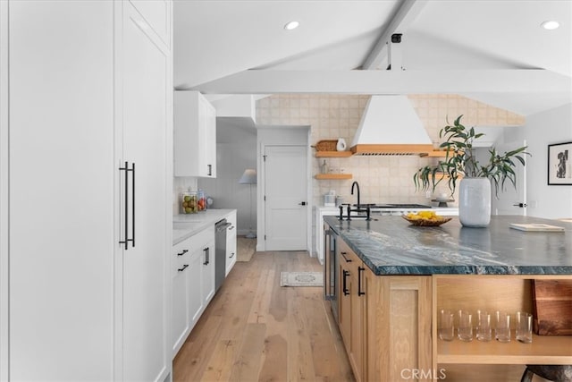 kitchen featuring light wood-type flooring, white cabinetry, stainless steel dishwasher, custom range hood, and decorative backsplash