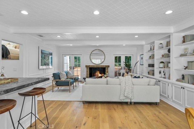 living room featuring plenty of natural light, built in shelves, light wood-type flooring, and crown molding