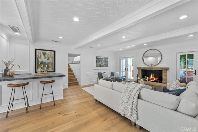 living room with beamed ceiling, crown molding, light hardwood / wood-style flooring, and french doors