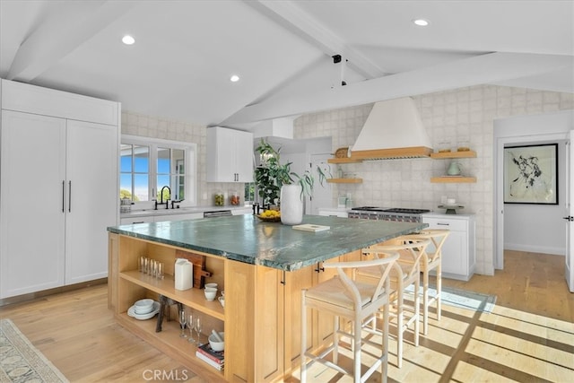 kitchen with light wood-type flooring, a spacious island, lofted ceiling with beams, white cabinets, and premium range hood