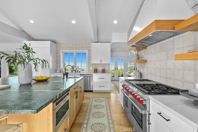 kitchen featuring a spacious island, white cabinetry, custom range hood, sink, and stainless steel appliances