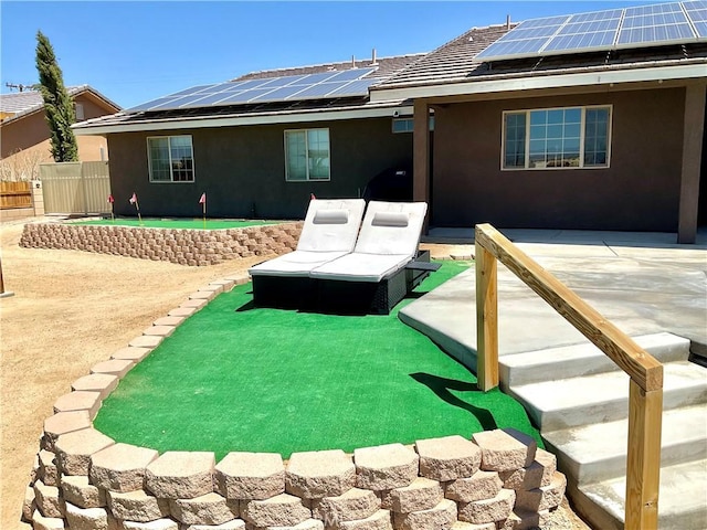 back of property with roof mounted solar panels, a patio, stucco siding, and fence