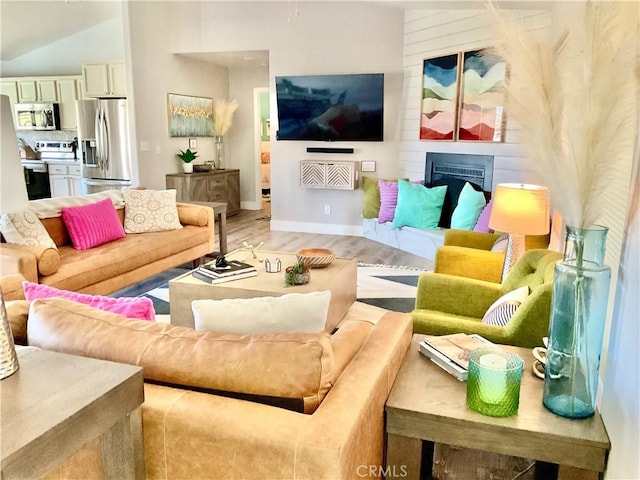 living area with baseboards, light wood-style floors, a fireplace, and vaulted ceiling