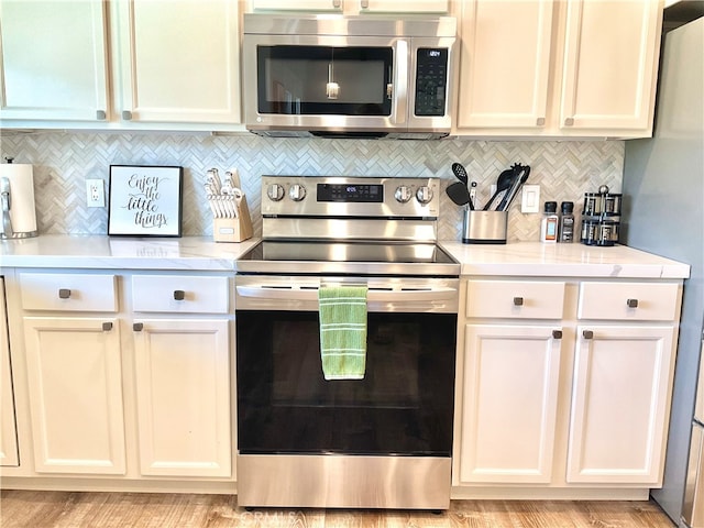 kitchen with white cabinetry, light stone counters, backsplash, stainless steel appliances, and light hardwood / wood-style flooring