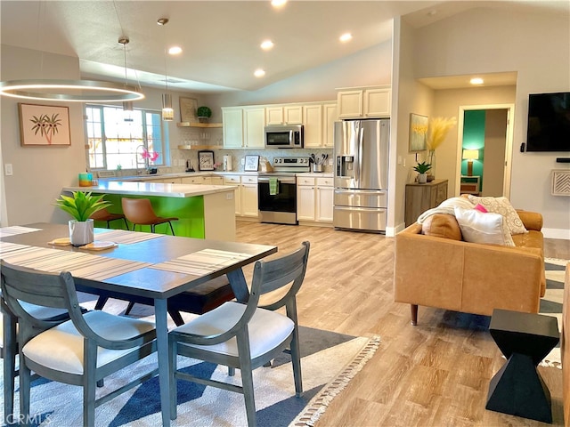 kitchen with pendant lighting, white cabinets, lofted ceiling, light hardwood / wood-style flooring, and appliances with stainless steel finishes