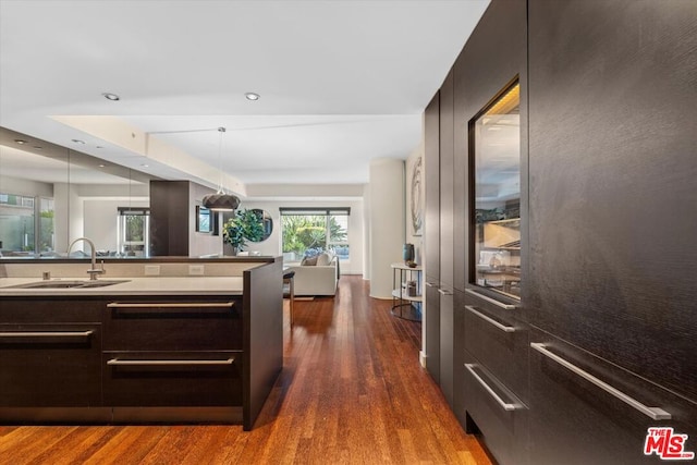 kitchen featuring sink, decorative light fixtures, a raised ceiling, and dark wood-type flooring