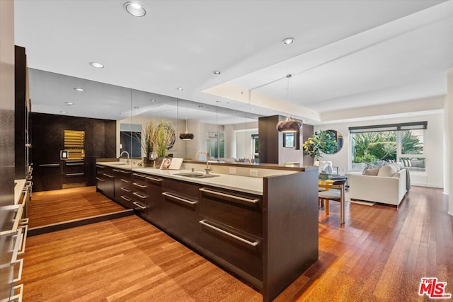 kitchen with pendant lighting, dark brown cabinets, hardwood / wood-style flooring, a kitchen island with sink, and sink