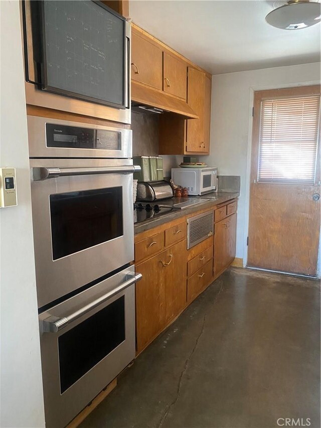 6161 Mirlo Rd, Yucca Valley, CA 92284 - kitchen with stainless steel double oven, brown cabinets, white microwave, concrete floors, and under cabinet range hood