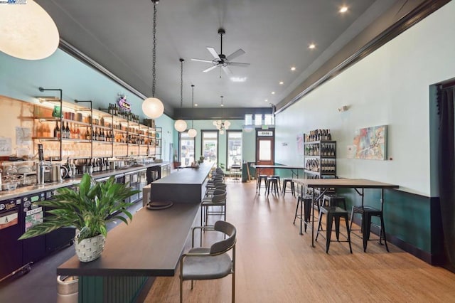 dining space with light wood-type flooring, a high ceiling, bar area, and ceiling fan