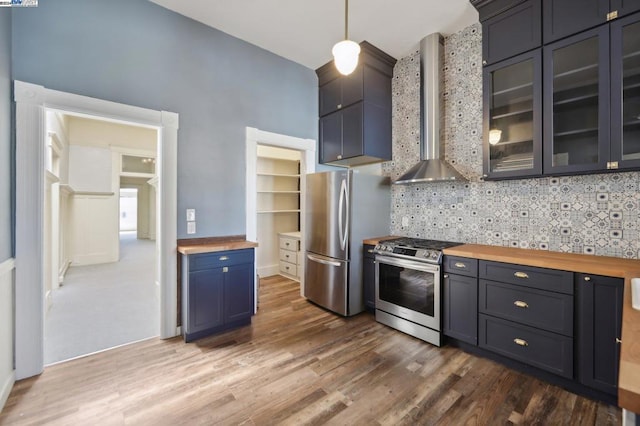 kitchen featuring butcher block counters, stainless steel appliances, decorative light fixtures, decorative backsplash, and wall chimney range hood