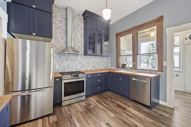 kitchen with dark hardwood / wood-style flooring, hanging light fixtures, stainless steel appliances, butcher block counters, and wall chimney range hood