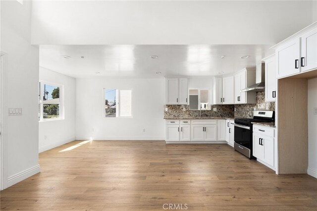 kitchen with wall chimney exhaust hood, light hardwood / wood-style floors, electric range, and white cabinetry