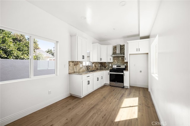 kitchen with light hardwood / wood-style flooring, white cabinetry, wall chimney range hood, and stainless steel range