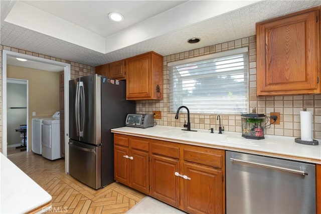 kitchen featuring tasteful backsplash, stainless steel appliances, light parquet floors, sink, and washing machine and clothes dryer