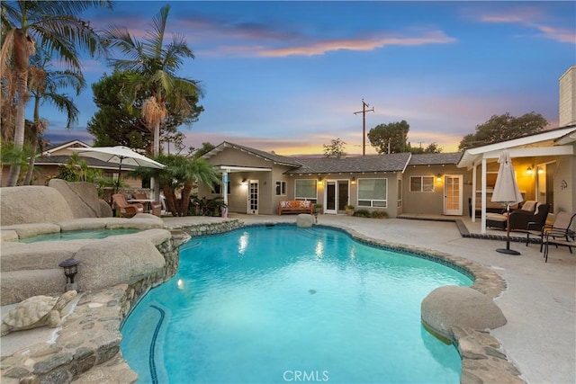 pool at dusk featuring an in ground hot tub and a patio