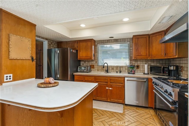 kitchen with a raised ceiling, sink, appliances with stainless steel finishes, kitchen peninsula, and light parquet flooring