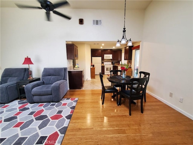 dining room with ceiling fan with notable chandelier, light hardwood / wood-style floors, and a high ceiling